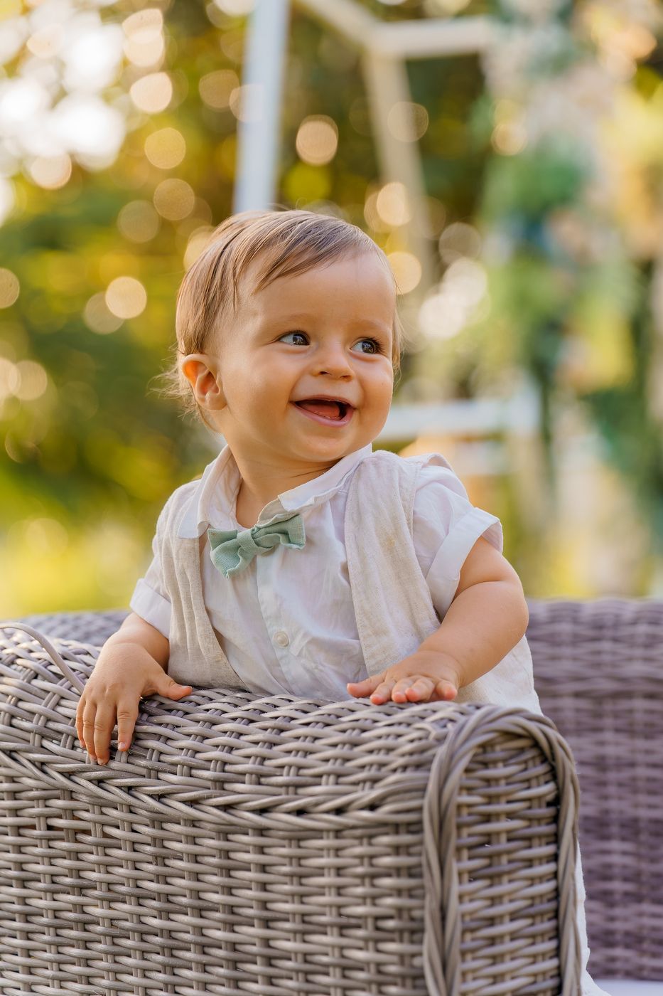 Baby smiling, leaning on a wicker armchair