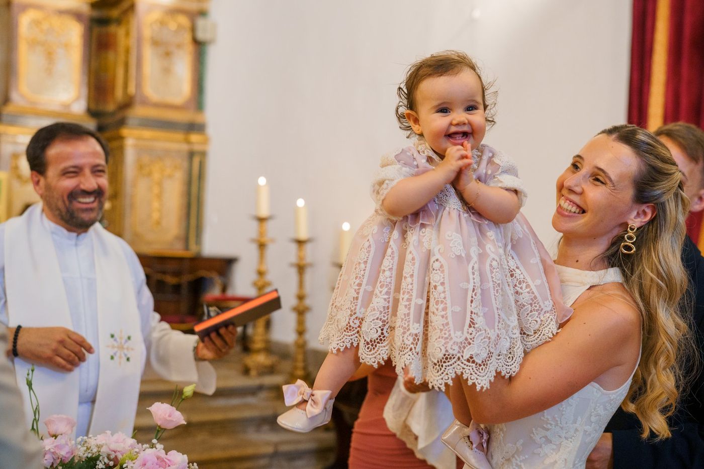 Baby laughing in mum's arms, with the priest