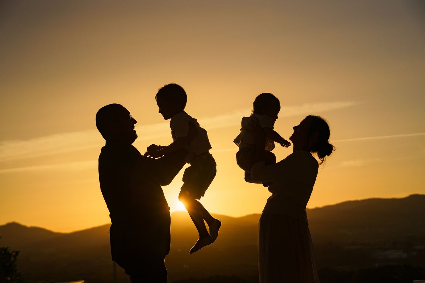 Family silhouetted at sunset, lifting the children up