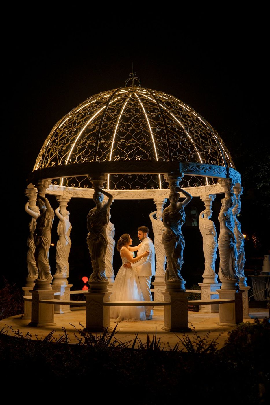 Bride and groom in a lit bandstand at night