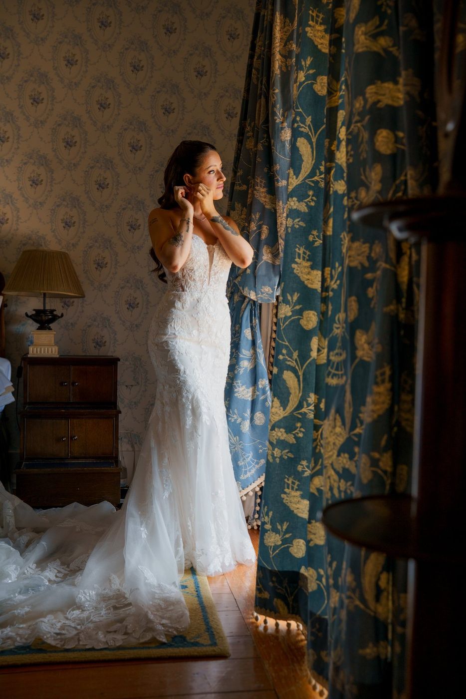 Bride putting on an earring by the curtain