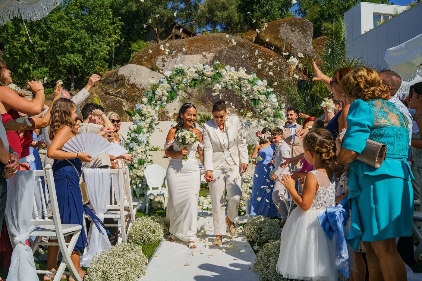 The couple leaving the ceremony, among guests and a flower arch