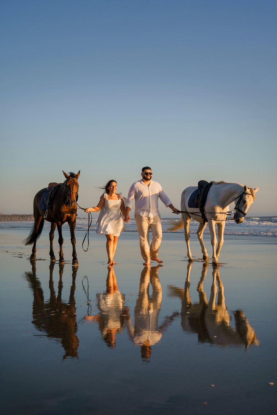 Couple with two horses on the beach, with reflection