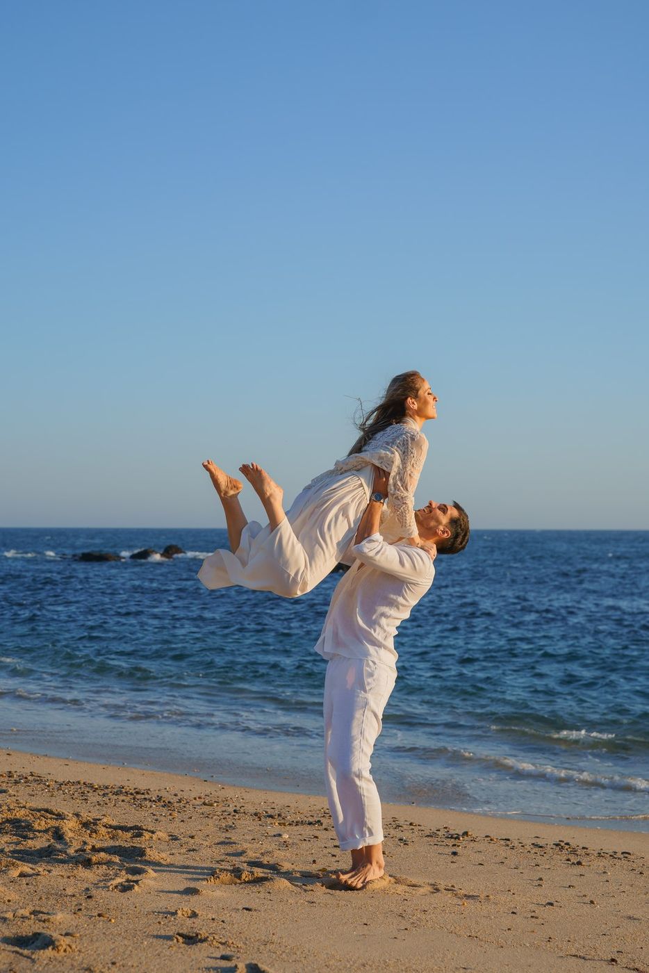 He lifts her into the air by the sea