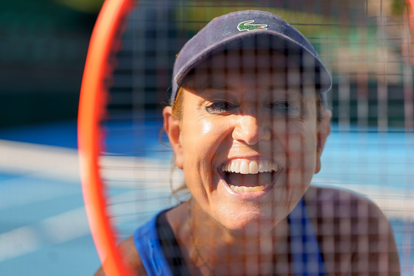 Player smiling through her racket at a tennis tournament