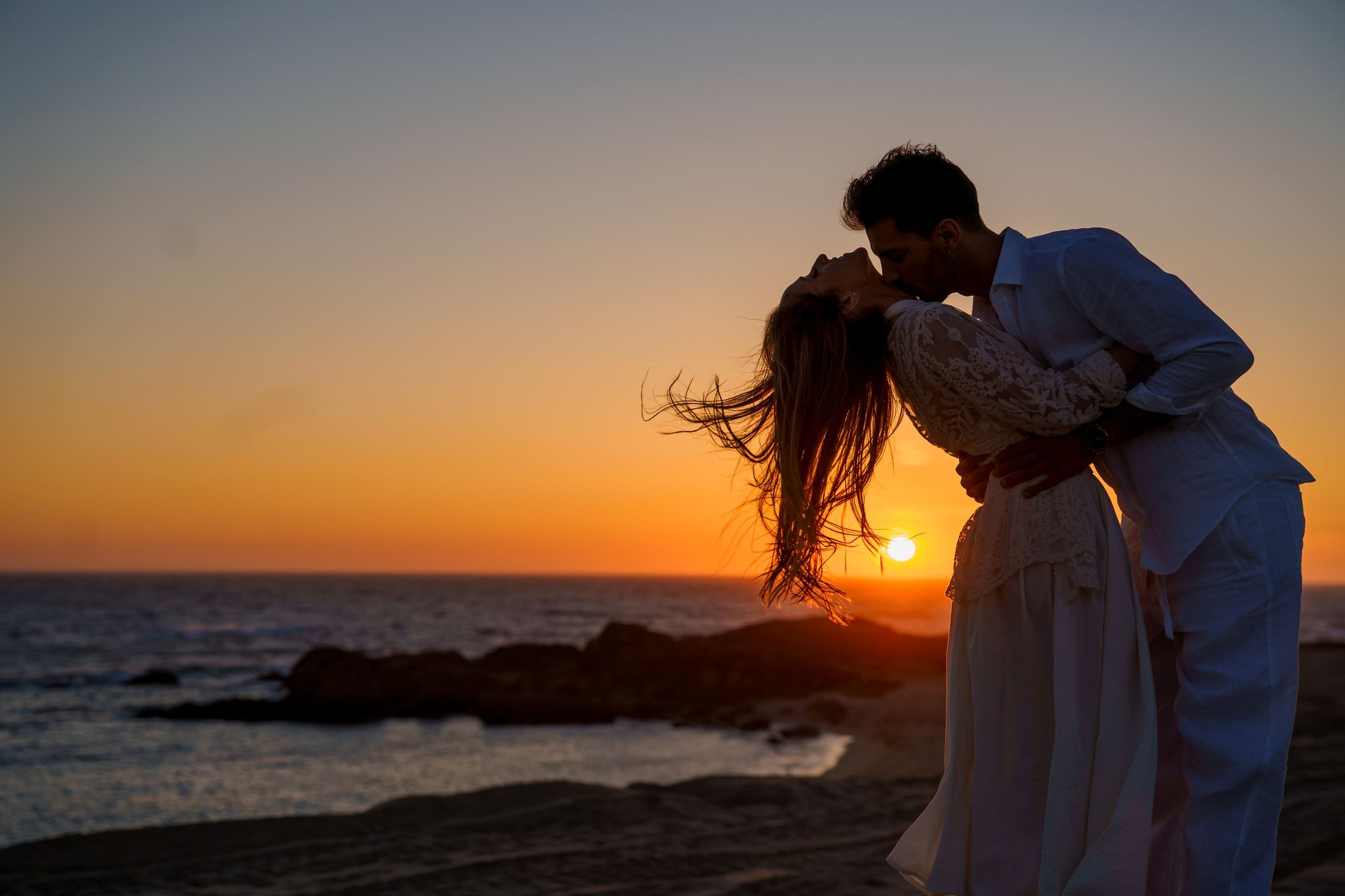 Couple silhouetted kissing at sunset by the sea