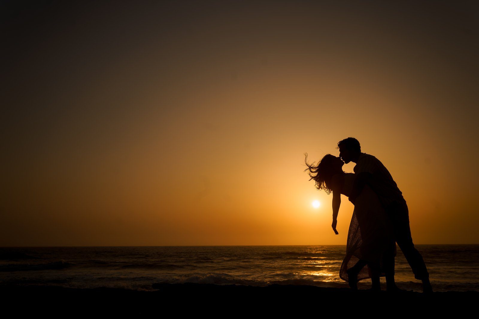 Couple silhouetted at sunset by the sea