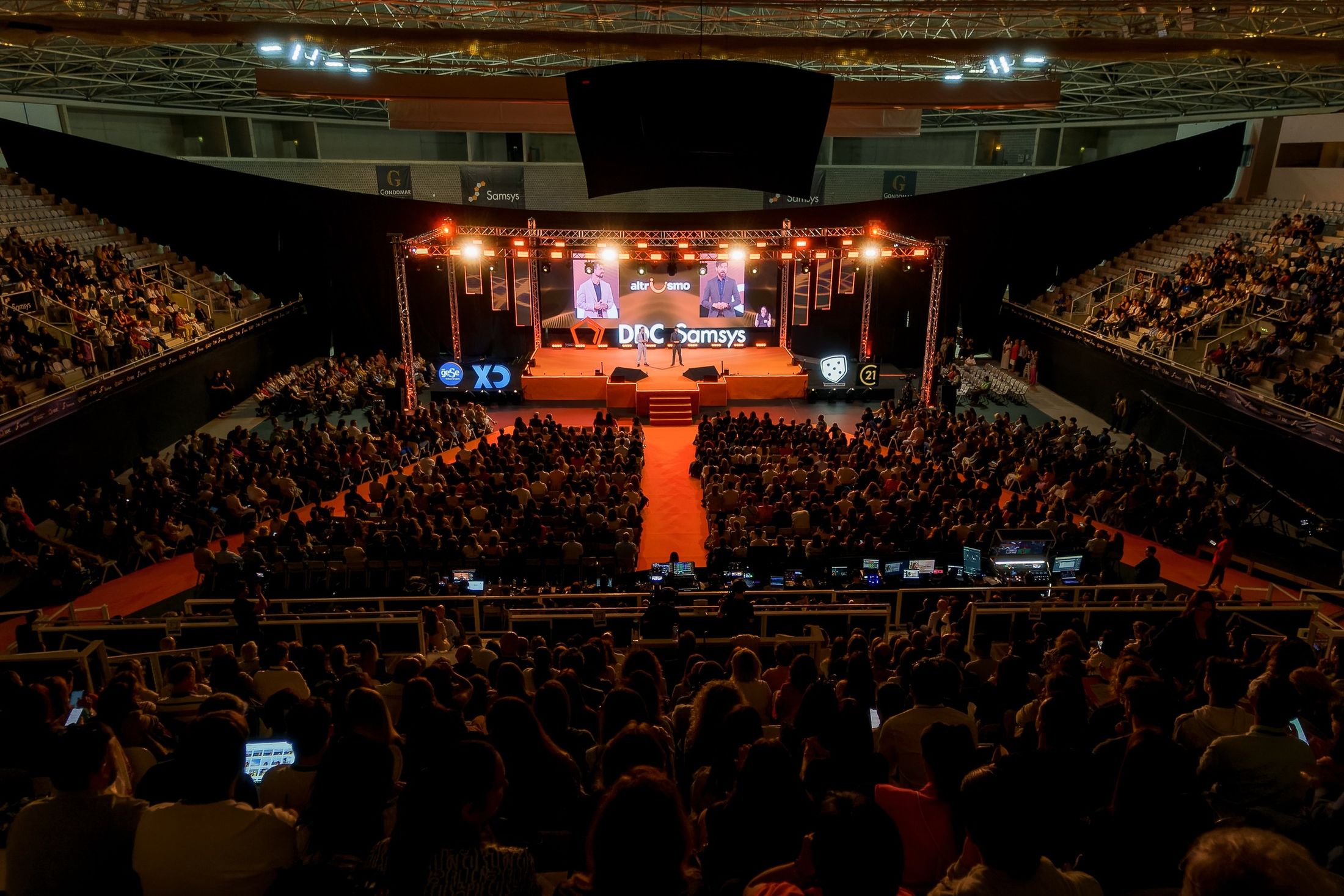 Large conference in an arena, with a lit stage and a full audience